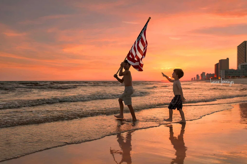 Two boys on beach at sunset with the American flag