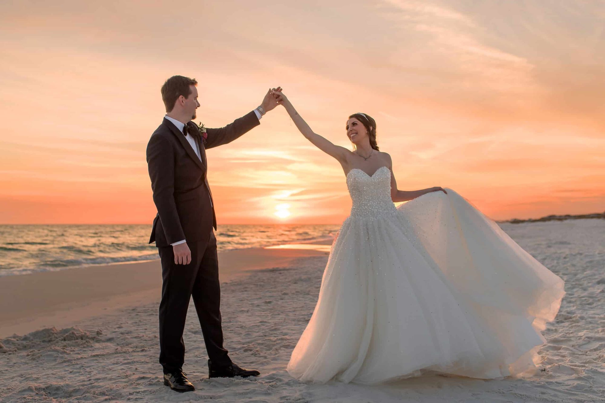 A bride and groom in their wedding attire on the beach at sunset