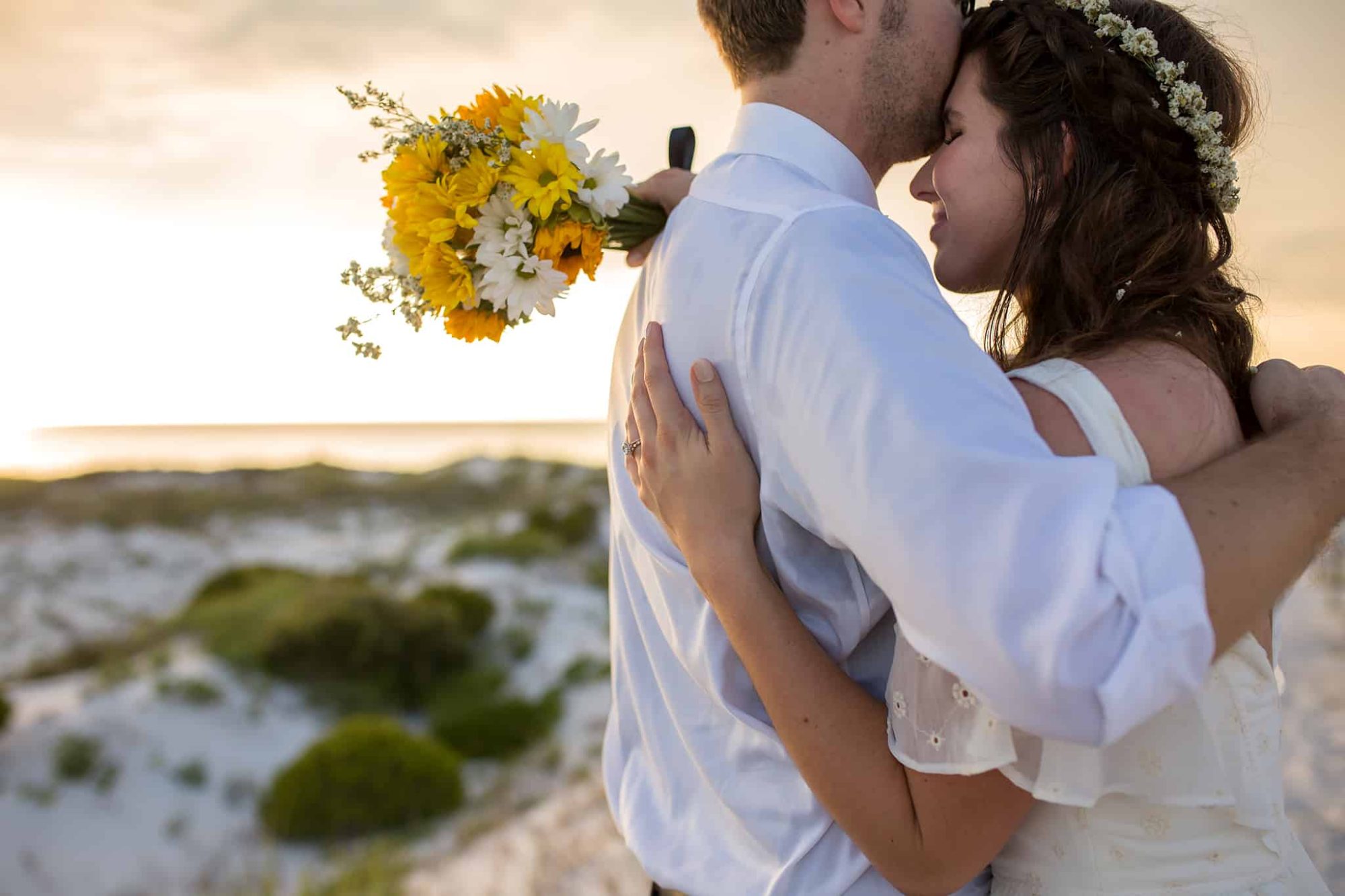 Close up of a husband and wife holding each other while the bride clasps a wedding bouquet in one hand