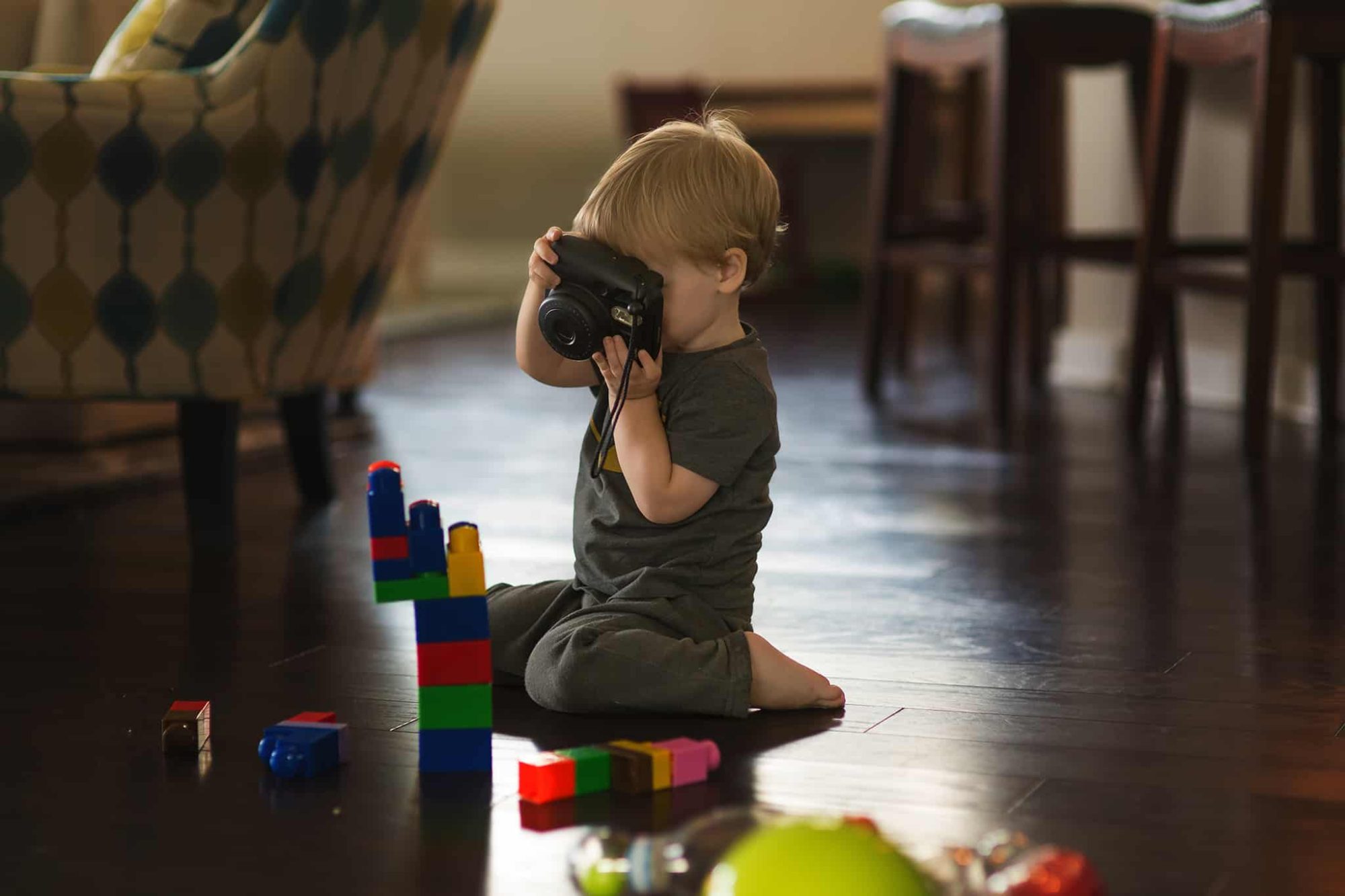 A young child sitting on the floor, playing with giant lego and a camera