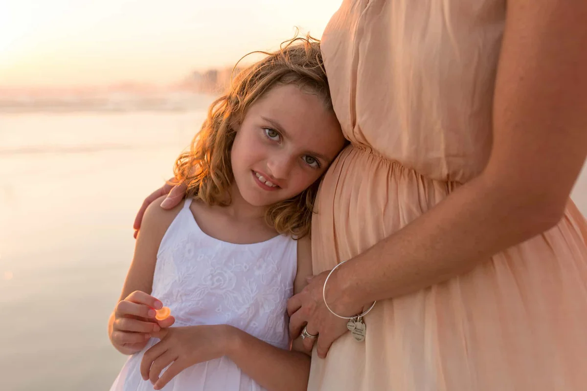 Young girl with her mother and beach in background.