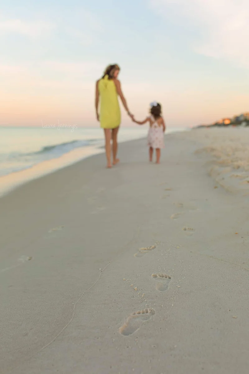 Mother and young daughter holding hands, walking along the water's edge at the beach