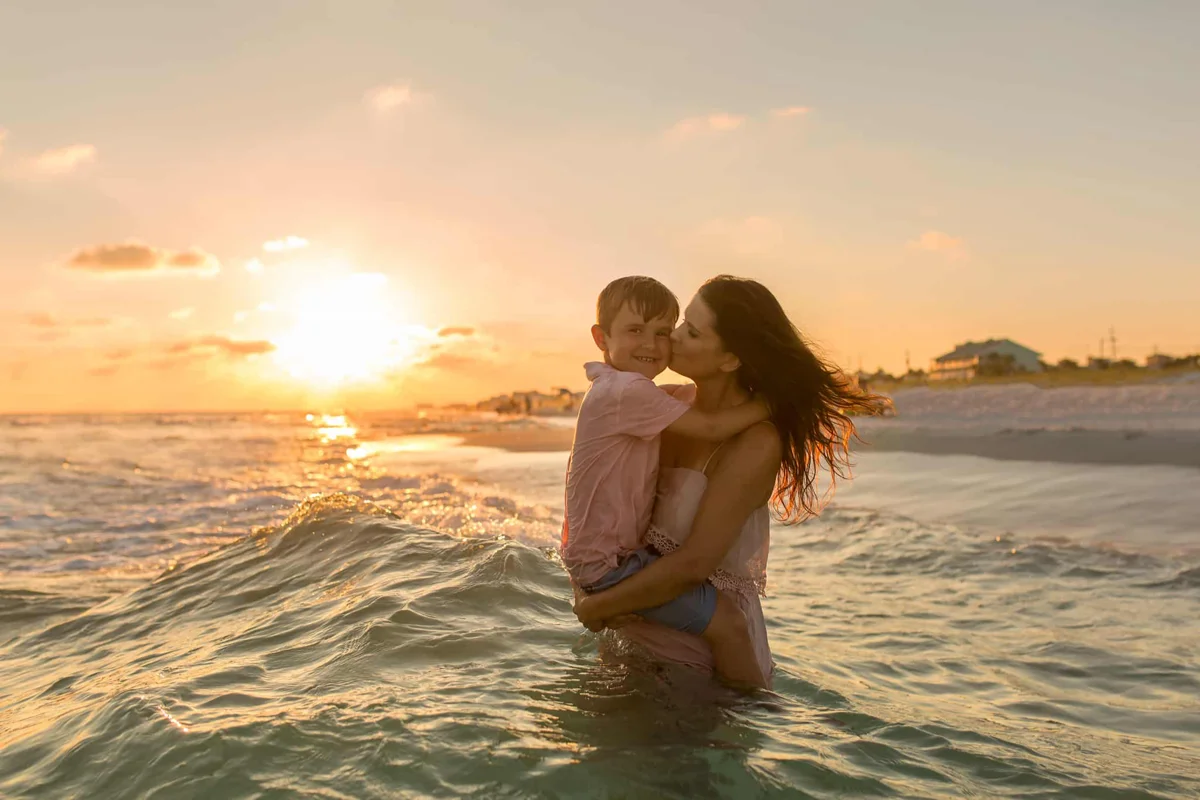 A mother holding her young son in the ocean waves, kissing his cheek