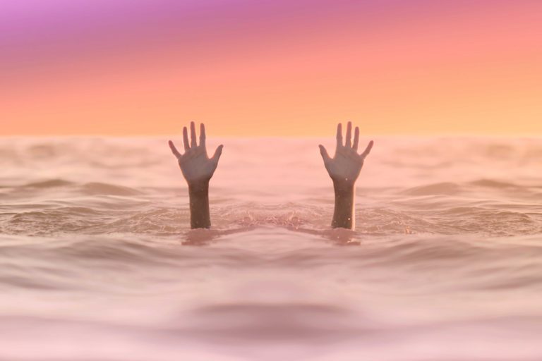 A child below the water surface, raising their hands out of the water, towards a sunset sky