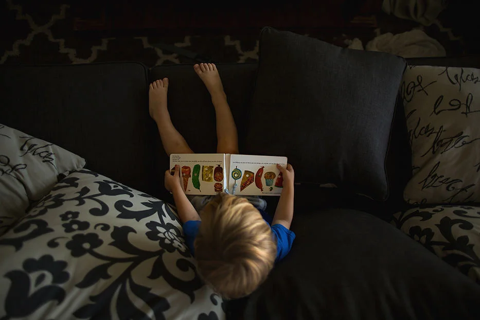 A top down overhead view of a child sitting on a couch reading a book.