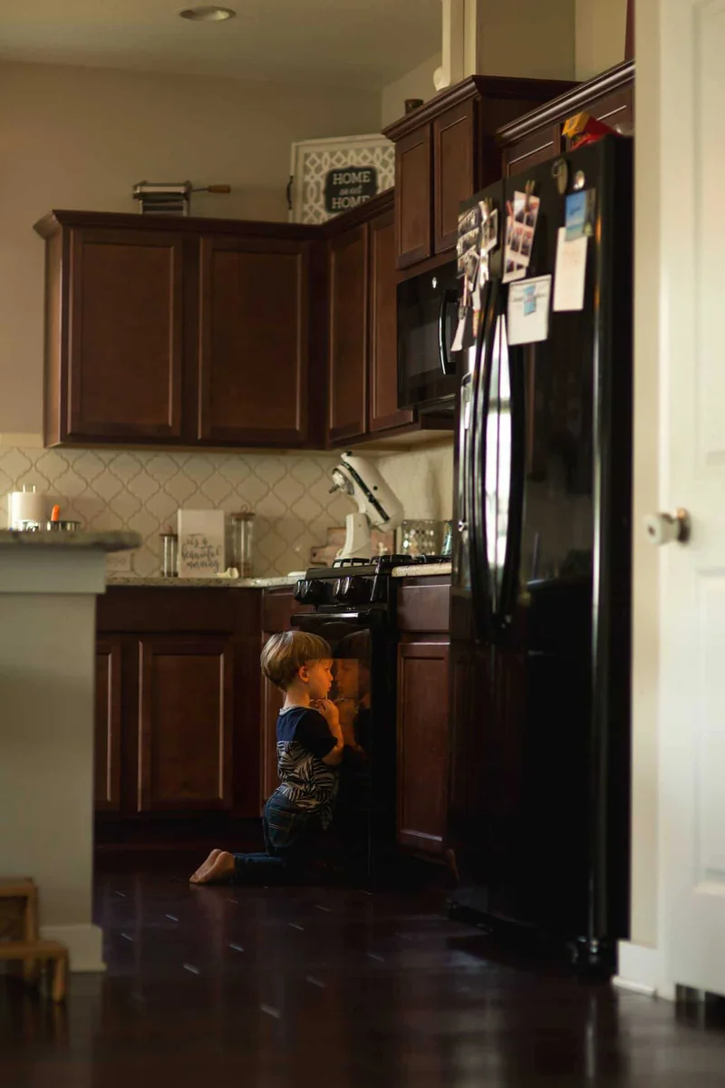 A young boy in the kitchen, staring into the oven, waiting for something to finish cooking,