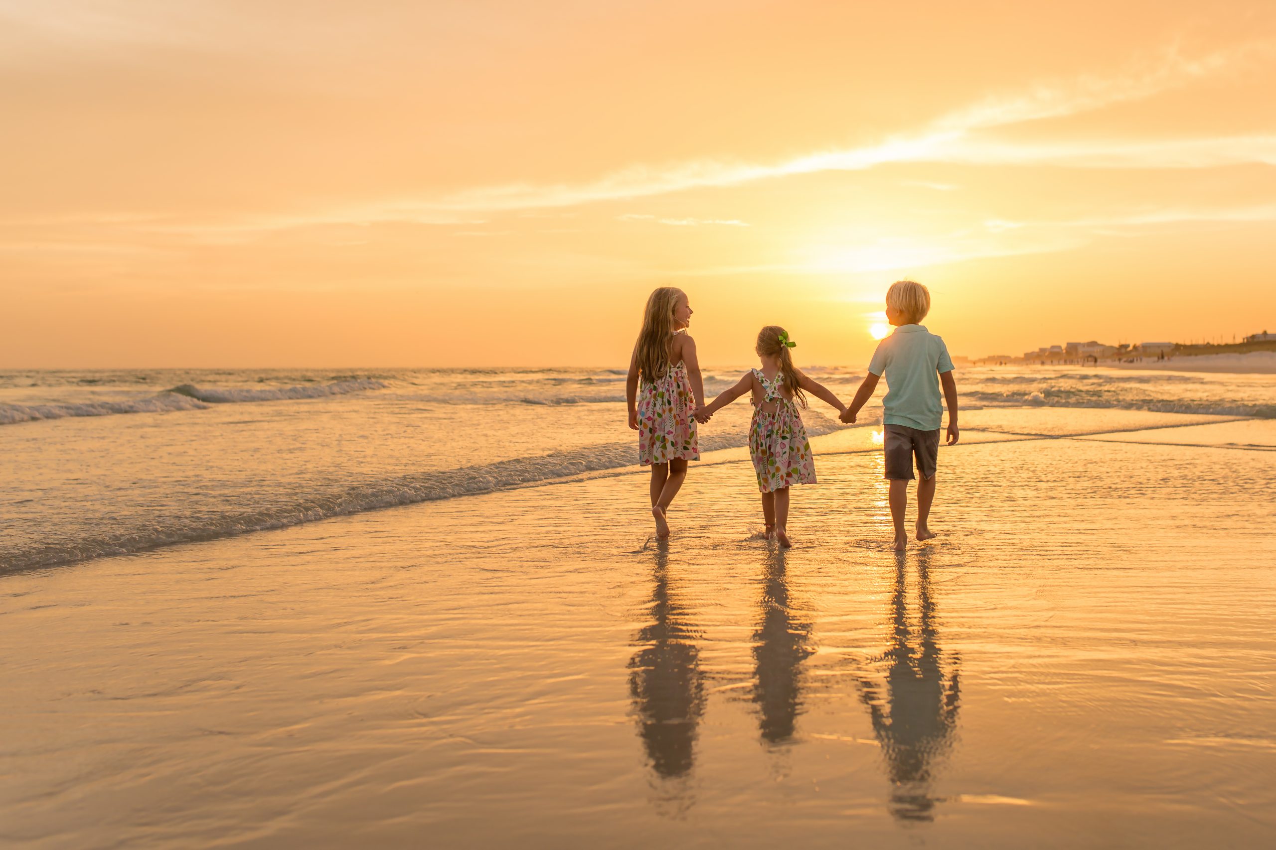 3 children on Panama City Beach, facing away from the camera, walking towards the sunset